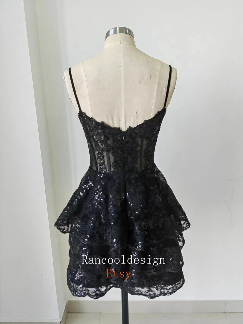 May include: Black short dress with a layered skirt and lace detailing. The dress has a fitted bodice and spaghetti straps. The dress is made of a sheer fabric with sequins throughout. The dress is shown on a mannequin. The text "Rancooldesign Etsy" is visible on the dress.