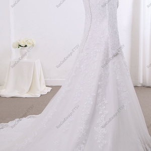 May include: A white wedding dress with long sleeves and a lace overlay. The dress has a fitted bodice and a flowing skirt with a train.
