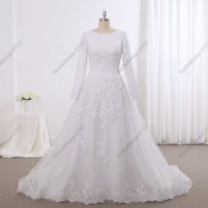 May include: A white wedding dress with long sleeves and a lace bodice. The skirt is full and flowing, and the dress has a modest neckline.