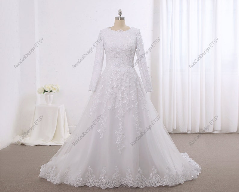 May include: A white wedding dress with long sleeves and a lace bodice. The skirt is full and flowing, and the dress has a modest neckline.
