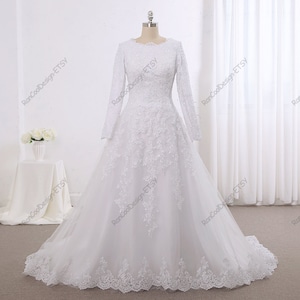 May include: A white wedding dress with long sleeves and a lace bodice. The dress has a full skirt and a train.