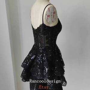 May include: A black short dress with a lace bodice and a layered skirt. The skirt has a ruffled design and is adorned with sequins. The dress is on a mannequin and the text "Rancooldesign Etsy" is visible at the bottom.