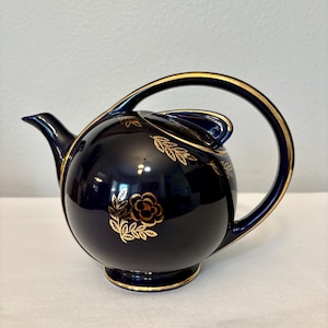 May include: A cobalt blue teapot with a gold trim and floral design. The teapot has a rounded body and a curved handle.