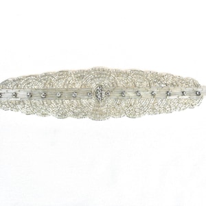 May include: A long, horizontal hair barrette featuring intricate silver beadwork arranged in concentric circular patterns. The design includes a central horizontal bar accented with small, clear, sparkling crystals that extend across the entire length of the piece.