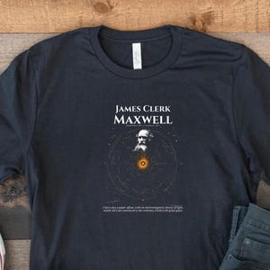 Może przedstawiać: Ciemnoniebieska koszulka z grafiką Jamesa Clerka Maxwella i tekstem. Grafika zawiera diagram układu słonecznego. Koszulka jest połączona z niebieskimi dżinsami i białymi trampkami.