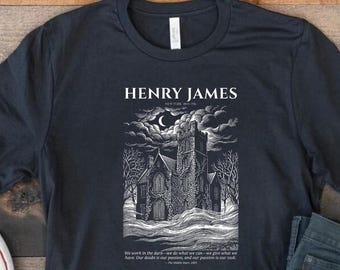 May include: A dark charcoal gray short-sleeve t-shirt featuring a white graphic print of a gothic mansion under a crescent moon. The text reads HENRY JAMES and includes a quote from The Middle Years, 1893, positioned below the illustration.