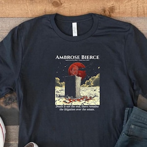 May include: Dark navy blue t-shirt featuring a graphic from Ambrose Bierce's work. The design includes an illustration with the text "Death is not the end; there remains the litigation over the estate." The shirt is paired with blue jeans and white sneakers.