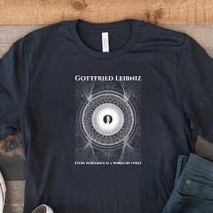 Peut inclure: T-shirt bleu marine foncé avec le texte "Gottfried Leibniz" au-dessus d'un graphique blanc et gris. Le graphique est un motif circulaire avec une figure centrale. En dessous, le texte "Every substance is a world by itself."