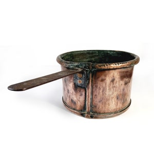 Può includere: Una pentola di rame antica con un manico di legno. La pentola ha una finitura martellata e una patina verde.