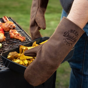 May include: Brown leather oven mitts with a "Best Daddy" design. The mitts are being used to hold a baking dish with potatoes.