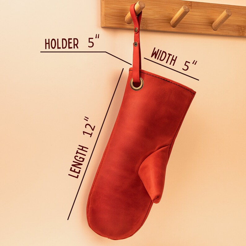 May include: Red leather oven mitt hanging on a wooden rack. The mitt is 12 inches long and 5 inches wide. It has a loop for hanging and a hole for a finger.
