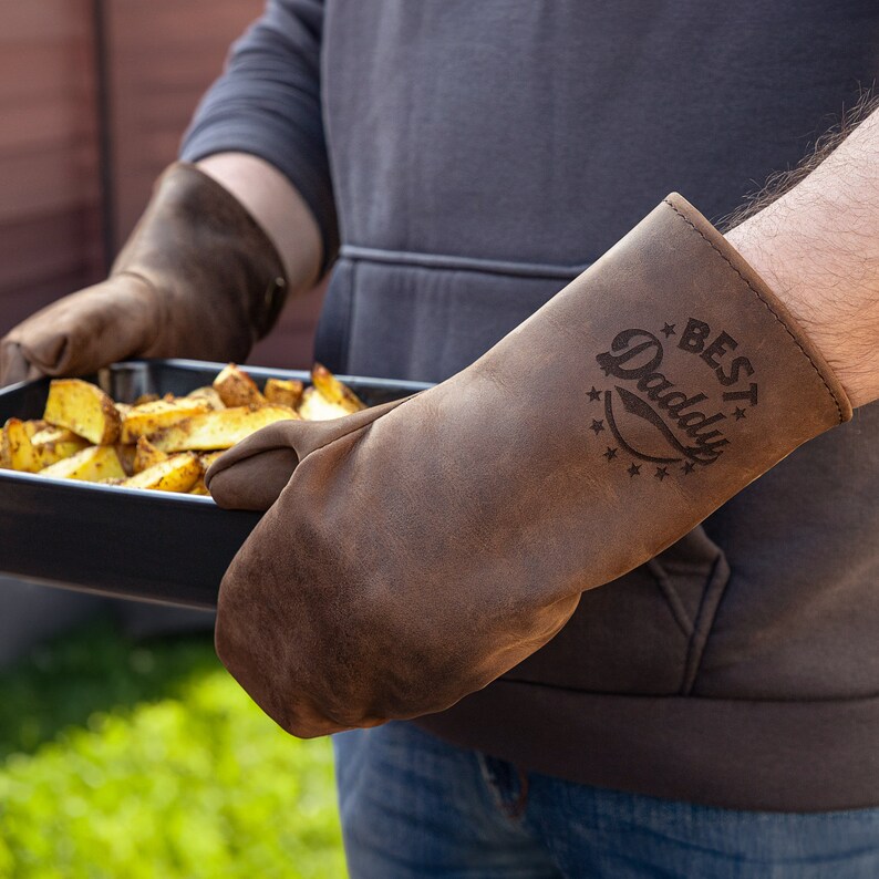 May include: Brown leather oven mitt with the text "BEST Daddy" in a vintage style font.