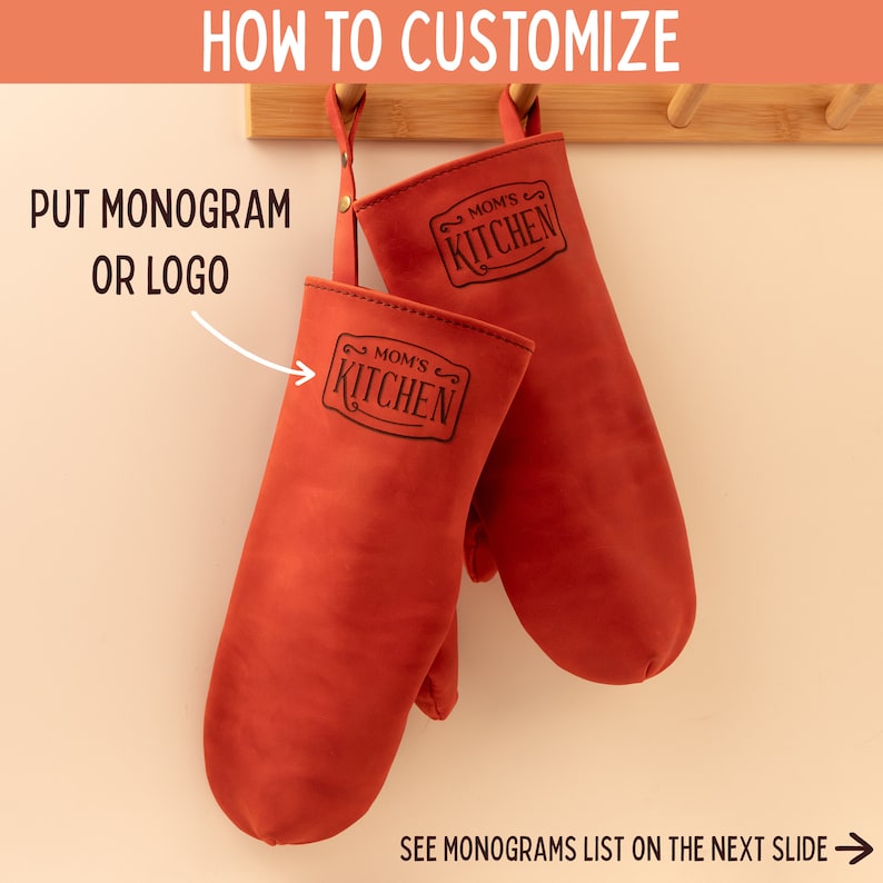 May include: Two red leather oven mitts with black text that reads "Mom's Kitchen" hanging on a wooden rack.  The text is in a decorative script font.