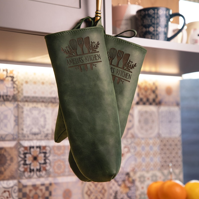 May include: A pair of green leather oven mitts with the text "Amelia's Kitchen" and "_s Kitchen"  engraved on them.