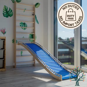 May include: A wooden climbing frame and slide for children. The ladder is fixed to the wall, and the slide has a blue surface. The set is made of light-coloured wood and is designed for indoor use. Decorative leaf stickers are on the wall.