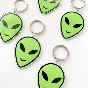 May include: Five green alien face keychains with silver key rings. Each keychain features a green alien face with black eyes and a smile.