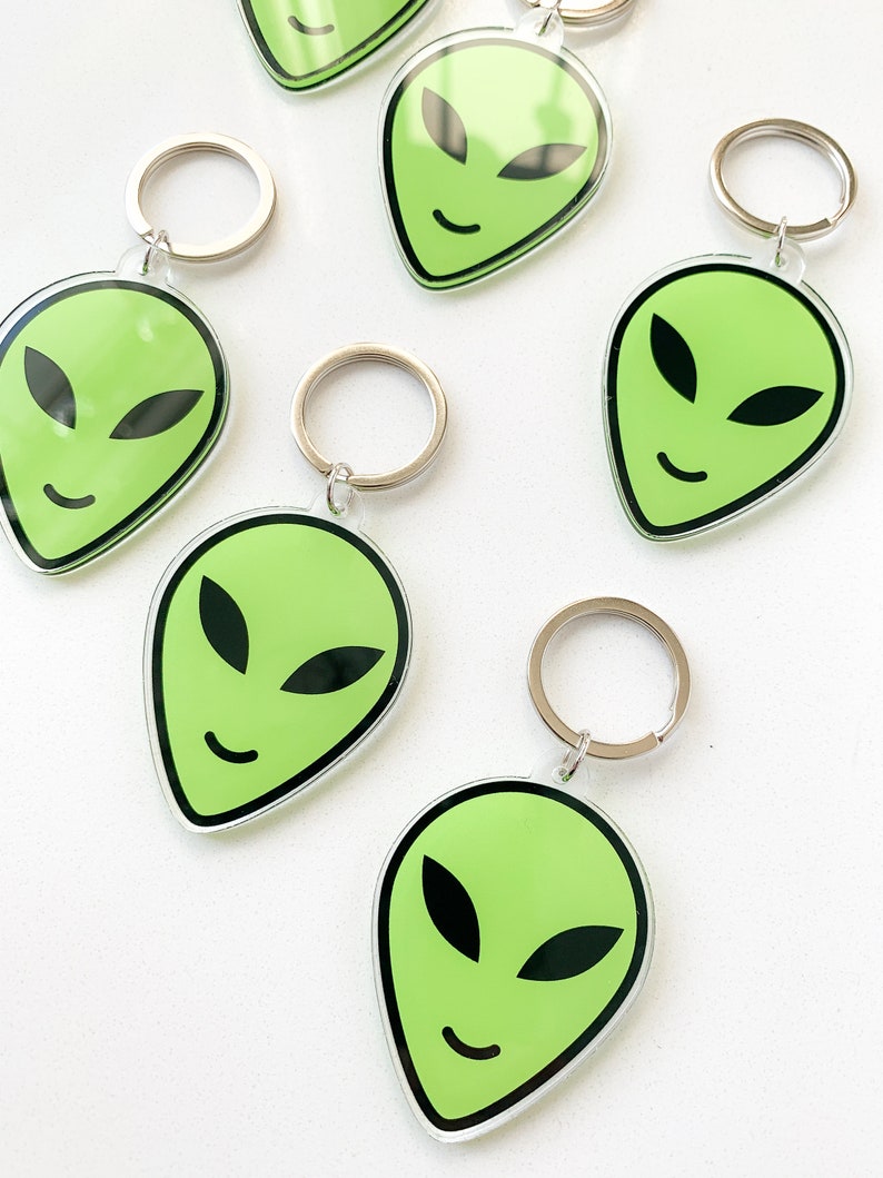 May include: Five green alien face keychains with silver key rings. Each keychain features a green alien face with black eyes and a smile.