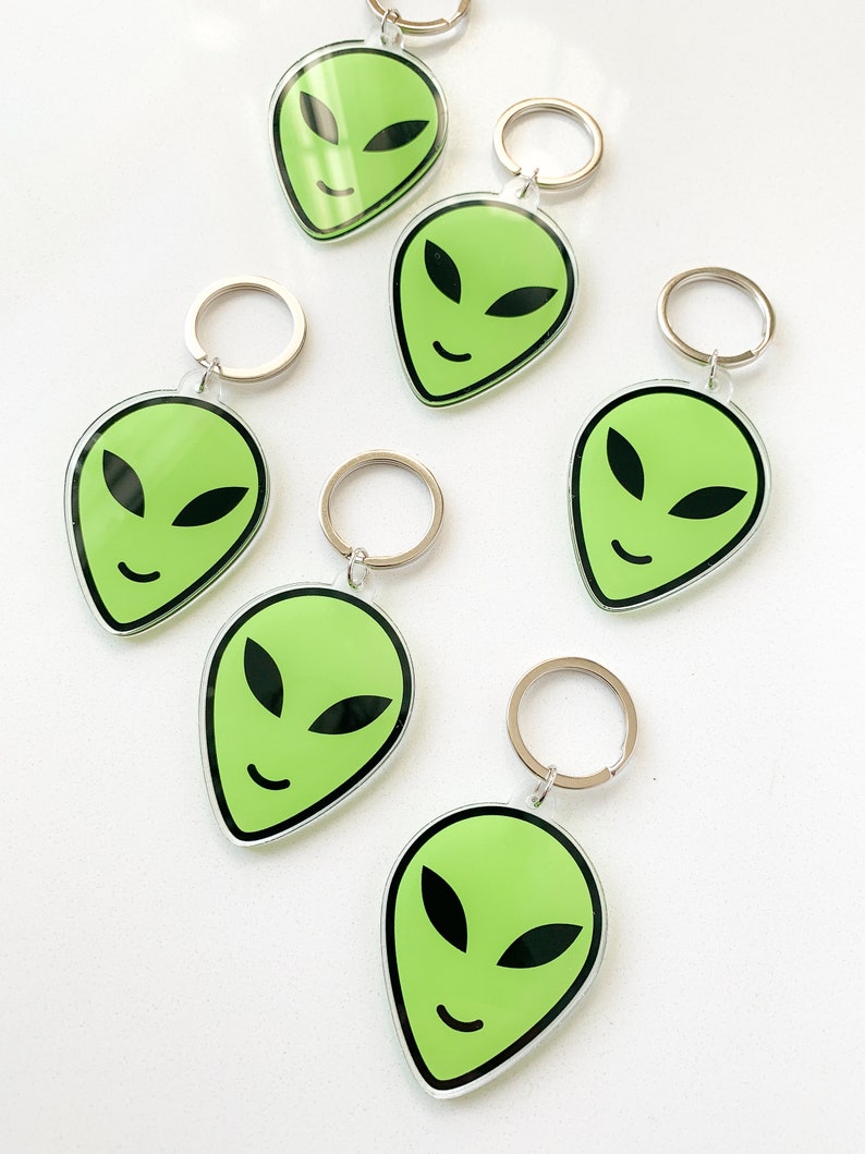 May include: Six green alien face keychains with silver key rings. Each keychain features a green alien face with black eyes and a smile.