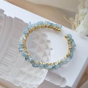 May include: A gold wire wrapped bracelet with light blue aquamarine stones. The bracelet is on a white surface.