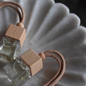 May include: Two small glass bottles with wooden caps and brown cords. The bottles are filled with a clear liquid and are sitting on a white marble surface.