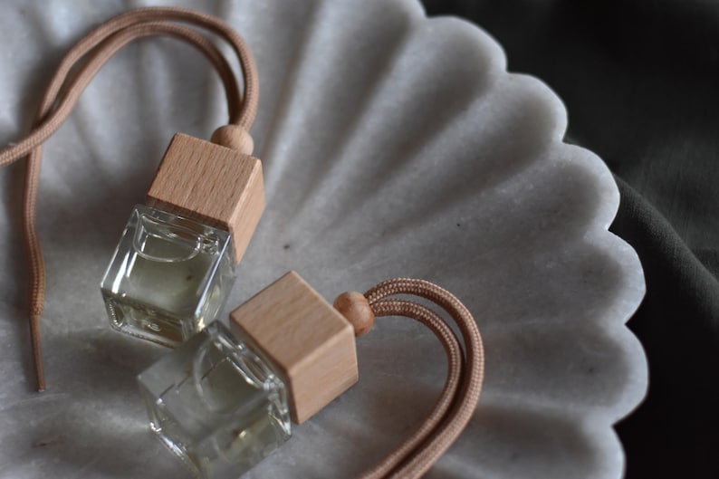 May include: Two small glass bottles with wooden caps and brown cords. The bottles are filled with a clear liquid and are sitting on a white marble surface.