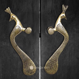 May include: A pair of gold peacock door handles with intricate details. The handles are mounted on a black wooden door.