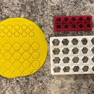 May include: Three cookie cutters, one red, one white and one yellow, with a star-shaped design. The cutters are used to make cookies or other pastries.
