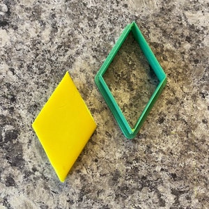 May include: A green plastic diamond-shaped cookie cutter and a yellow diamond-shaped piece of fondant.