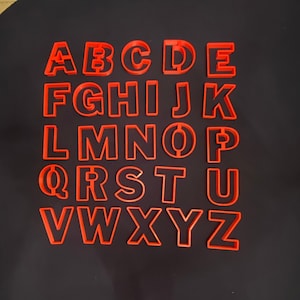 May include: A set of 26 red plastic alphabet cookie cutters. The cutters are arranged in alphabetical order from A to Z.