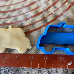 Pu&ograve; includere: Un tagliapasta di plastica blu a forma di furgone, accanto a un biscotto tagliato a forma di furgone.