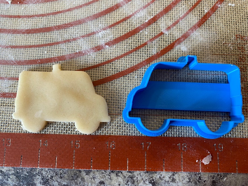 Pu&ograve; includere: Un tagliapasta di plastica blu a forma di furgone, accanto a un biscotto tagliato a forma di furgone.