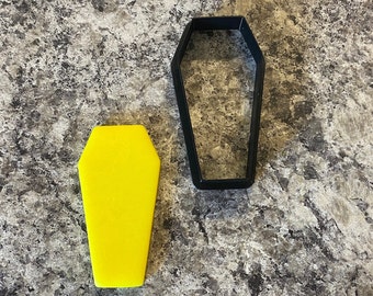 May include: A yellow plastic coffin cookie cutter and a black plastic coffin cookie cutter.