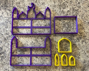 May include: Purple plastic cookie cutters shaped like a mosque with a crescent moon on top and a rectangular frame. There are also six smaller yellow cookie cutters shaped like arches.