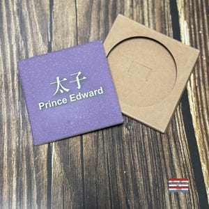 以下が含まれることがあります： 太子 Prince Edwardと白文字で書かれた紫色の正方形のプレート。プレートは、円形の切り抜きのある茶色の段ボール箱の隣の木製表面の上に置かれています。
