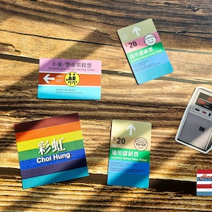 Puede incluir: Un conjunto de billetes de metro MTR de Hong Kong coloridos con diferentes tipos de tarifas y precios. Los billetes presentan un diseño de arcoíris, un billete para niños/estudiantes, un billete de valor común y un billete de 20 $. Los billetes están sobre una superficie de madera.