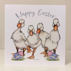 May include: A square Easter greeting card with the words "Happy Easter" in grey script. The card shows a watercolour illustration of four white ducks with orange beaks and feet, near Easter eggs.