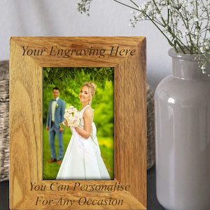 May include: A wooden picture frame with a light brown finish. The frame has a rectangular opening for a photo and is engraved with the text "Your Engraving Here" at the top and "You Can Personalise For Any Occasion" at the bottom.