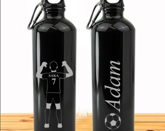 May include: Two black water bottles with a silver carabiner clip. One bottle has a soccer player silhouette with the text "SAKA 7" and the other bottle has the name "Adam" and a soccer ball graphic.