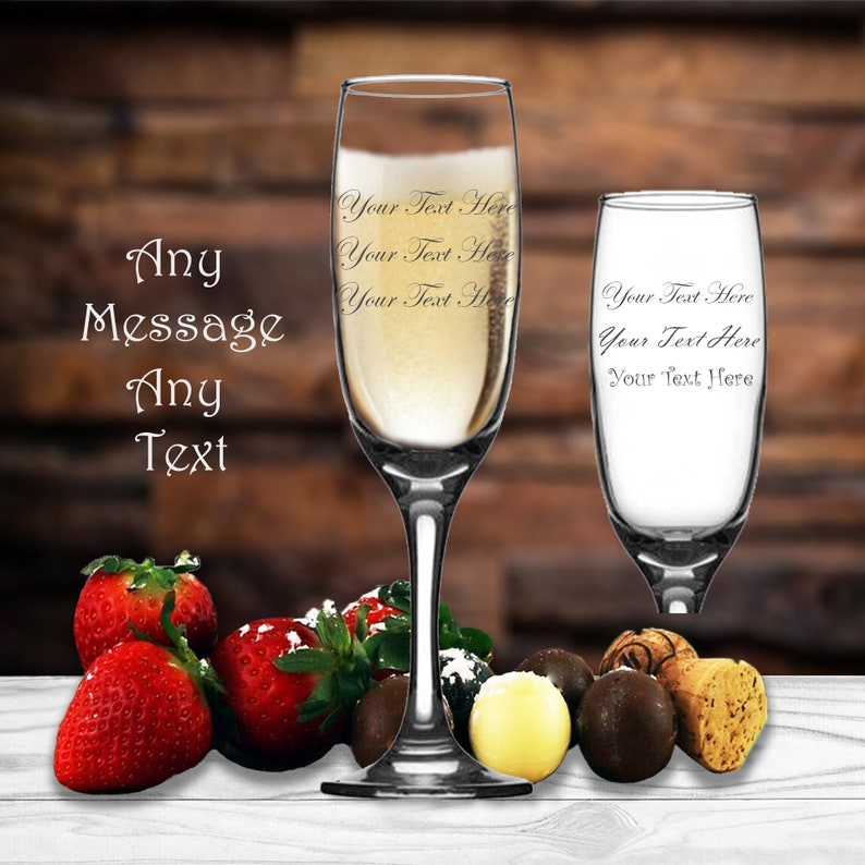May include: Two champagne flutes, one filled with champagne, with strawberries, chocolates, and a cork on a white wooden surface. The flutes are engraved with the text "Your Text Here".