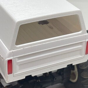 Peut inclure: Un plateau de camion blanc avec une benne rigide blanche et une lunette arri&egrave;re. La benne du camion est vide et la lunette arri&egrave;re est transparente. Le camion est sur une surface blanche.
