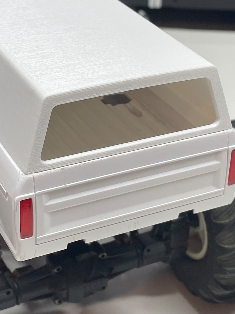 Peut inclure: Un plateau de camion blanc avec une benne rigide blanche et une lunette arri&egrave;re. La benne du camion est vide et la lunette arri&egrave;re est transparente. Le camion est sur une surface blanche.
