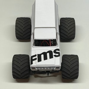 Peut inclure: Camion monster blanc avec des pneus noirs et un logo "FMS" noir sur le c&ocirc;t&eacute;.