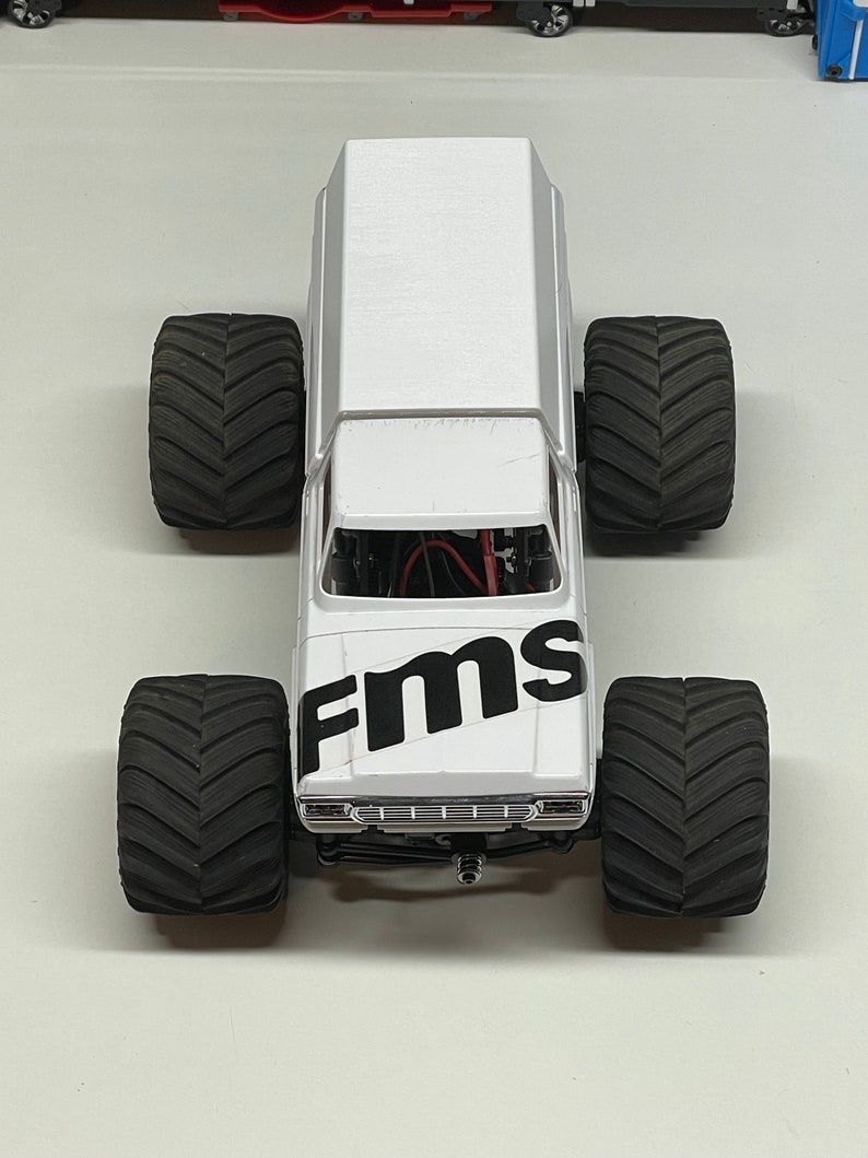 Peut inclure: Camion monster blanc avec des pneus noirs et un logo "FMS" noir sur le c&ocirc;t&eacute;.