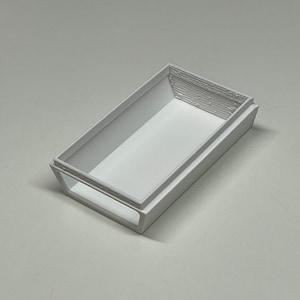Peut inclure: Une bo&icirc;te rectangulaire en plastique blanc avec un rebord sur&eacute;lev&eacute; autour du bord. La bo&icirc;te est vide et a une surface lisse.