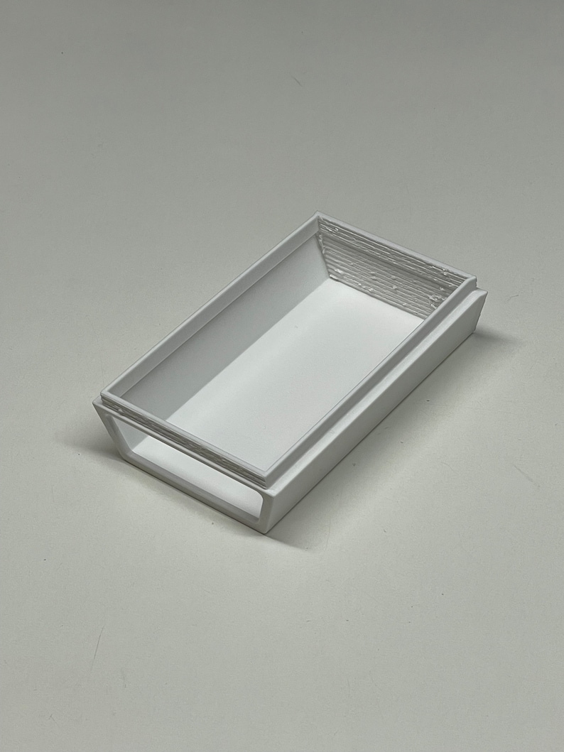 Peut inclure: Une bo&icirc;te rectangulaire en plastique blanc avec un rebord sur&eacute;lev&eacute; autour du bord. La bo&icirc;te est vide et a une surface lisse.