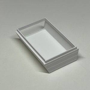 Peut inclure: Bo&icirc;te rectangulaire blanche avec un rebord sur&eacute;lev&eacute; autour du bord sup&eacute;rieur. La bo&icirc;te est en plastique blanc lisse.
