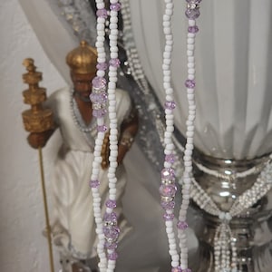 Puede incluir: Un collar de cuentas blancas con múltiples hilos y detalles de cristal morado.