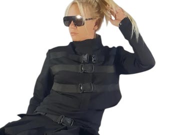May include: A black long-sleeved jacket featuring three horizontal straps with plastic buckle closures across the chest, paired with black trousers, a matching belt with a buckle, and black lace-up boots, worn with dark tinted sunglasses.