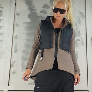 May include: A woman wearing a brown and black jacket with a black vest over it. She is wearing black pants and black platform boots. She is also wearing sunglasses.