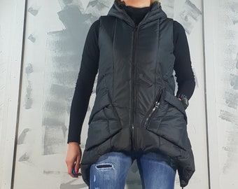 May include: A black puffer vest with a hood and zipper closure. The vest has a quilted design and a drawstring at the bottom. The person is wearing blue jeans and black and white platform shoes.